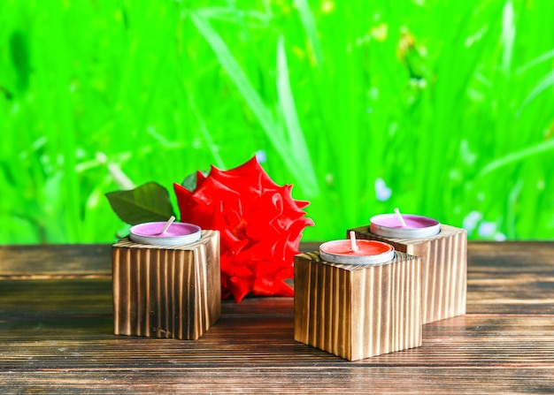 Closeup of wooden candle holders with tea light on red rose petals and blurred green background