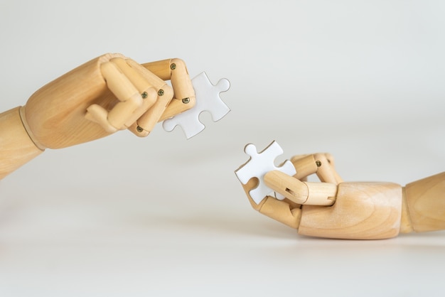 Closeup of wooden hand model holding puzzle jigsaw on white.