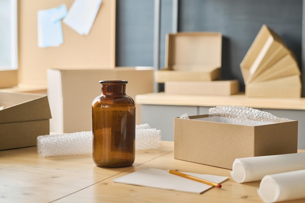 Closeup of workplace with glass bottle standing on it and opened cardboard boxes for packing parcels