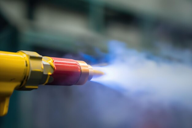 Photo closeup of yellow and red powder coating gun in action spray gun emits blue smoke factory or