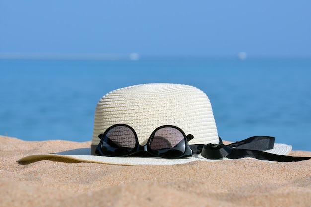 Closeup of yellow straw hat and black protective sunglasses on sandy beach at tropical seaside on warm sunny day. Summer vacation concept.