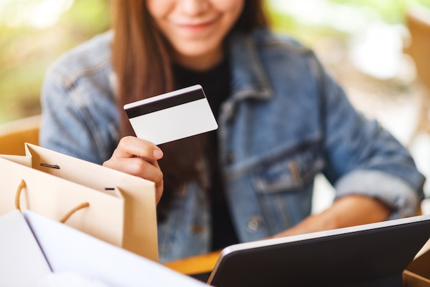 Closeup  of a young asian woman using tablet pc and credit card for online shopping with postal parcel box and shopping bags on the table