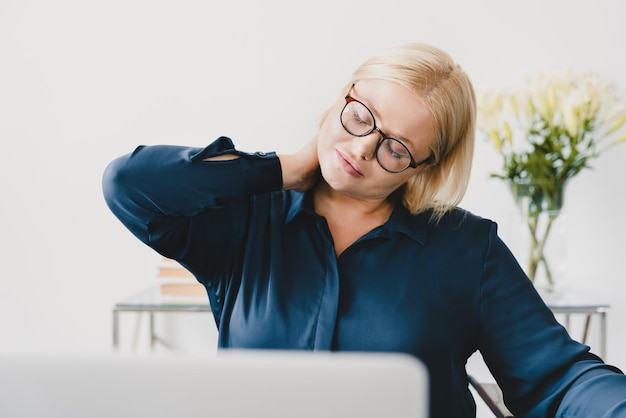 Photo closeup young caucasian tired sad businesswoman suffering from neck pain stretching rubbing her neck nerve spasm at workplace at office desk after sedentary occupation health problems