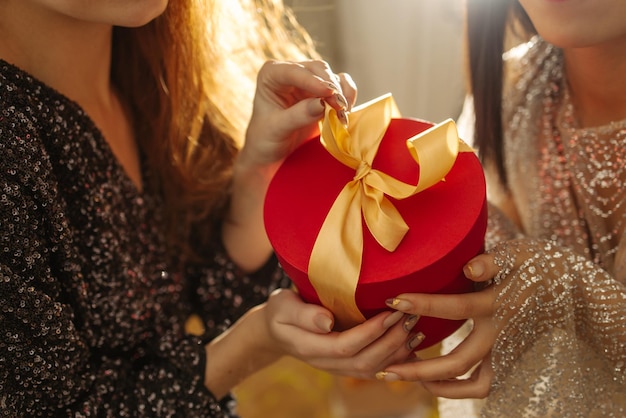 Closeup of young fairskinned female hands of two girls in dresses holding small gift box Holiday concept