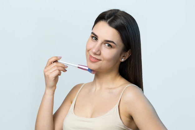 Closeup of a young girl in a light top on a white background making a facial makeup