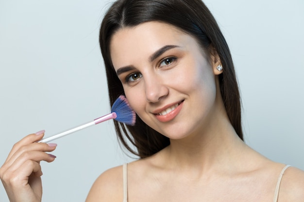 Closeup of a young girl in a light top on a white background making a facial makeup