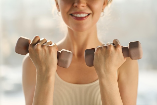 Closeup of young healthy woman exercising with dumbbells and smiling at camera