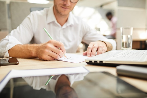 Closeup of young man sitting at table and drawing scheme on paper while working on design of project