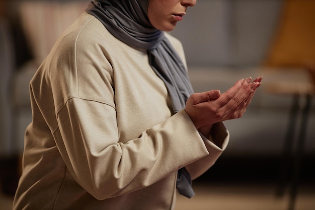 Closeup of young muslim woman in grey hijab and beige pullover saying prayer