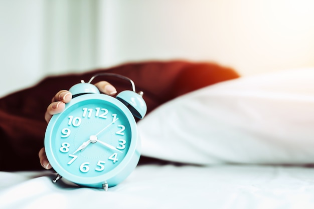 Closeup young sleeping woman and rise hand to turn off alarm clock in the bedroom at home.