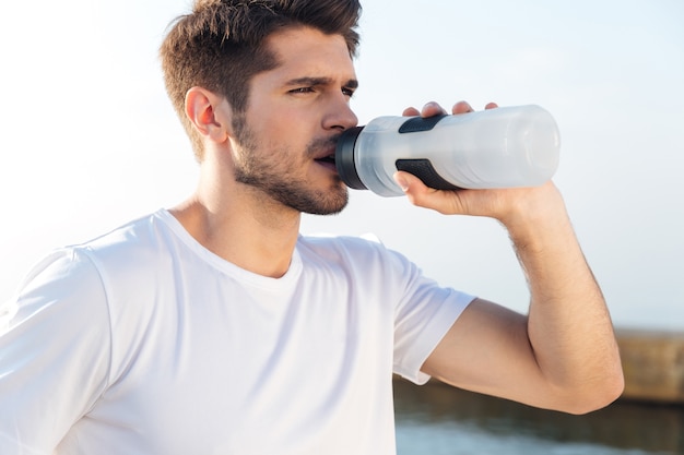 Closeup of young sportsman in white shirt drinking water outdoors