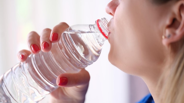 Closeup of young woman drinking water from plastic bottle