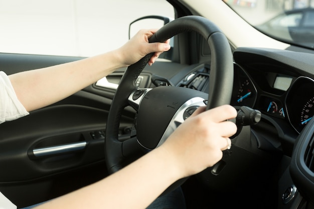 Closeup of young woman driving car and holding hands on steering wheel