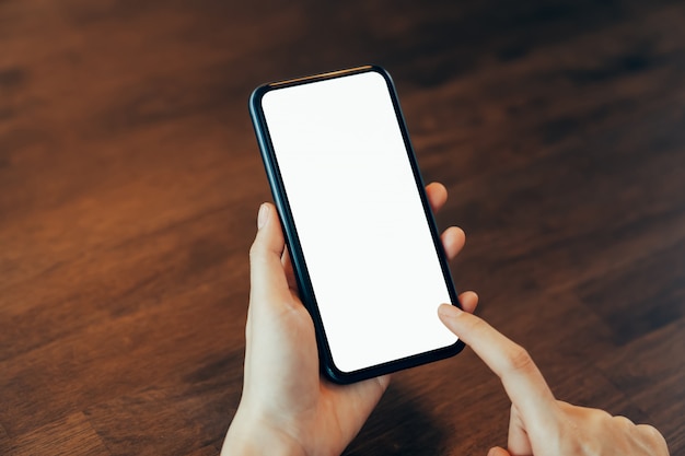 Closeup of young woman hand holding smartphone on the table and the screen is blank, social network concept.	