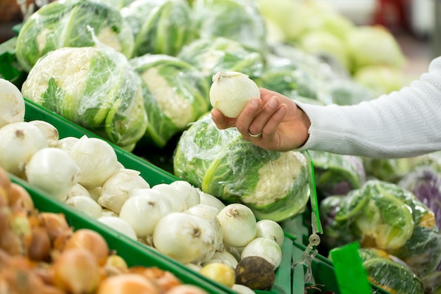 Closeup of young woman hand pick up onion on the basket in the supermarket