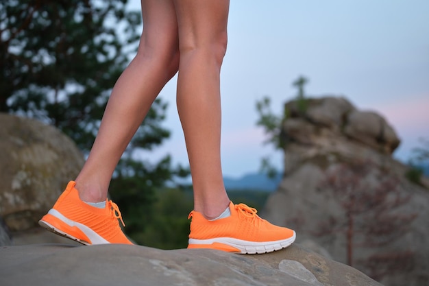 Closeup of young woman slim legs in bright orange sneaker shoes walking on mountain hiking trail in summer Active way of life and exercise on fresh air concept