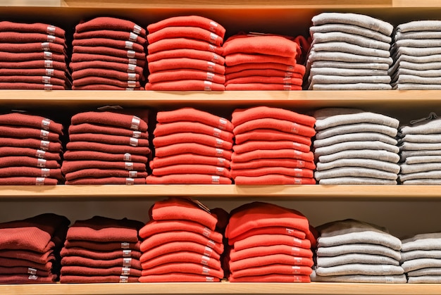 Clothes displayed in store. Lot warm sweaters of bright color are neatly stacked in a row on the store shelves. Piles of multicolored knitted woolen clothing. T-shirt on shelve.