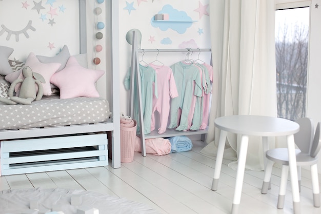 Clothes for little child hung in children room. Rack with hangers with baby clothes. Children cloth rack. Pastel color children clothes in a Row on Open Hanger indoors. Children's bedroom.  home decor