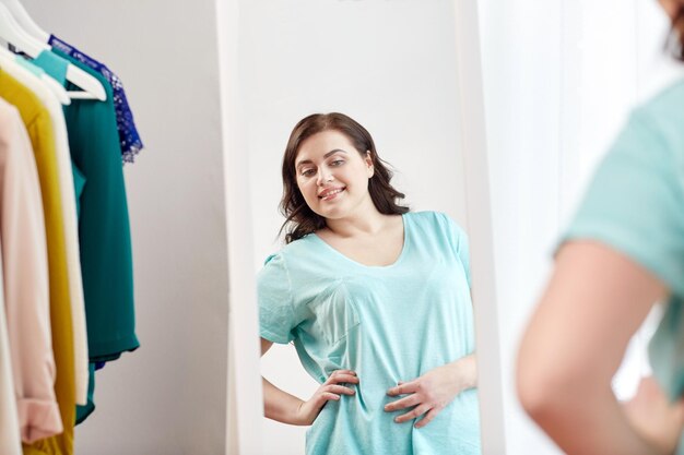 clothing, fashion, style and people concept - happy plus size woman choosing clothes and posing at mirror at home wardrobe