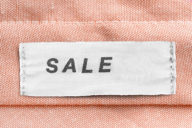 Clothing label says sale on beige textile background closeup