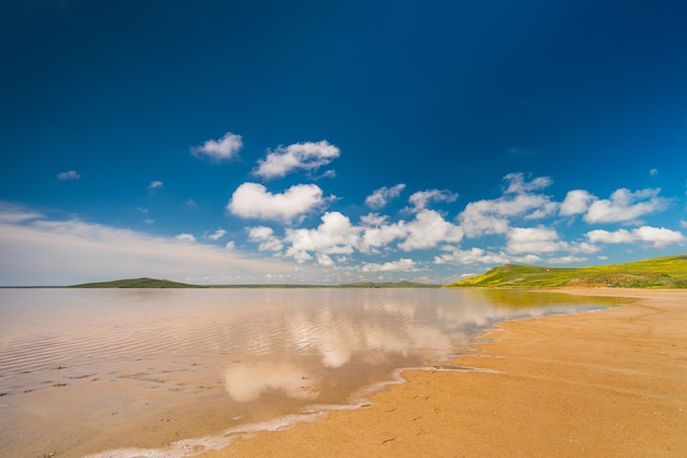 clouds in the blue sky are reflected in the water on the sandy shore