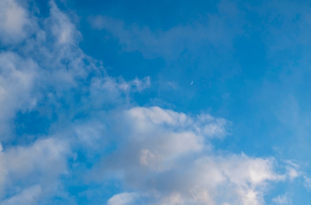 Clouds in a blue sky with a Crescent moon in the distance at sunset.