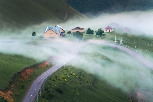 Clouds over the road and houses in the mountains in foggy evening