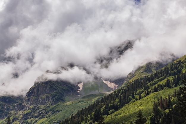 Clouds over the tops of the rocky mountains overgrown with trees