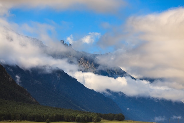 Clouds over the tops of the rocky mountains overgrown with trees