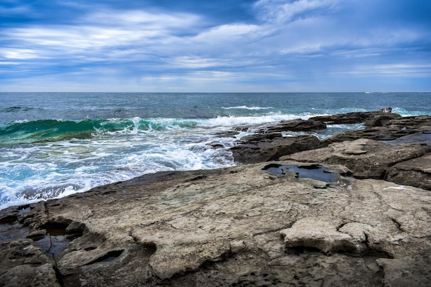 Cloudy sky over the sea turquoise waves crashing on the rocks