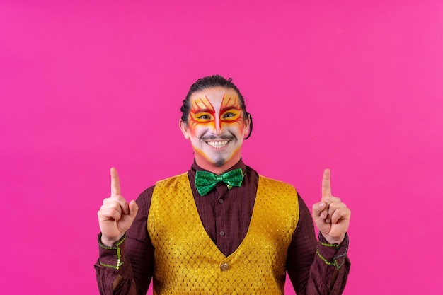 Clown with white face makeup showing empty space on pink background announcing something pointing up