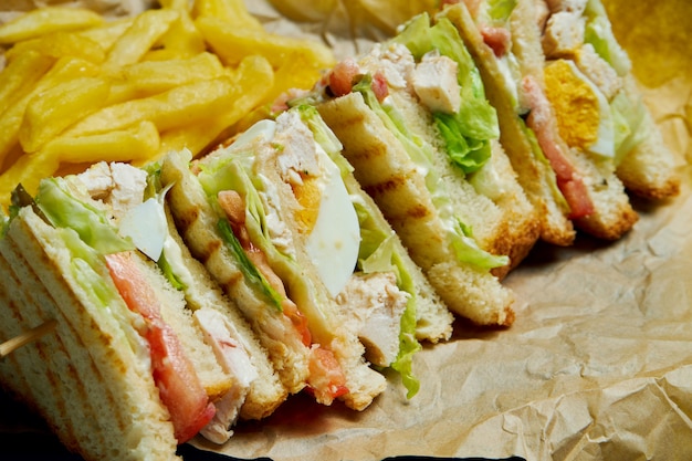 Club Sandwich with ham, tomatoes, pickled cucumber, egg, cheese and lettuce on a wooden tray. Close up. Tasty fast food. 