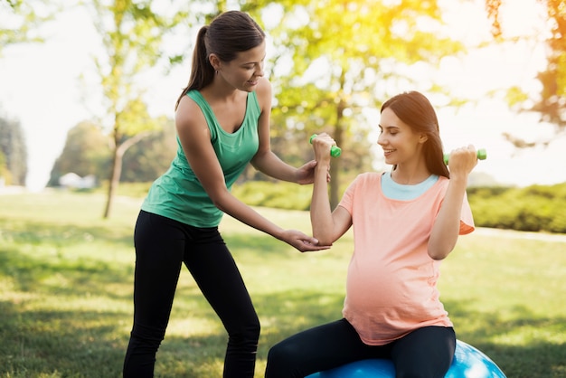 A coach helps a pregnant woman to do exercises 