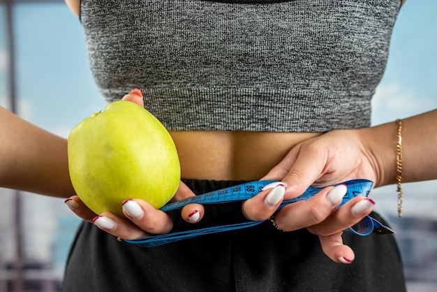 The coach holds a green apple in his hands and a measuring tape for measuring the body is wound on his hand Healthy lifestyle concept