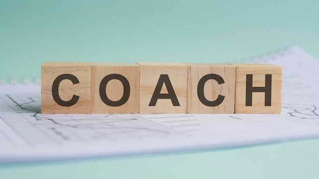 Coach is written on light wooden blocks. the word is located on a sheet with charts and graphs. business concept.