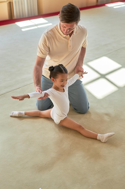 Coach supporting girl gymnast doing front split