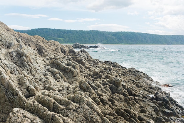 Coastal cliff formed by solidified lava closeup against the background of a distant sea shore