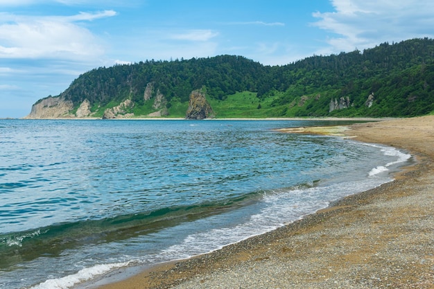 Coastal landscape pebble beach and beautiful wooded rocks on the green coast of Kunashir island