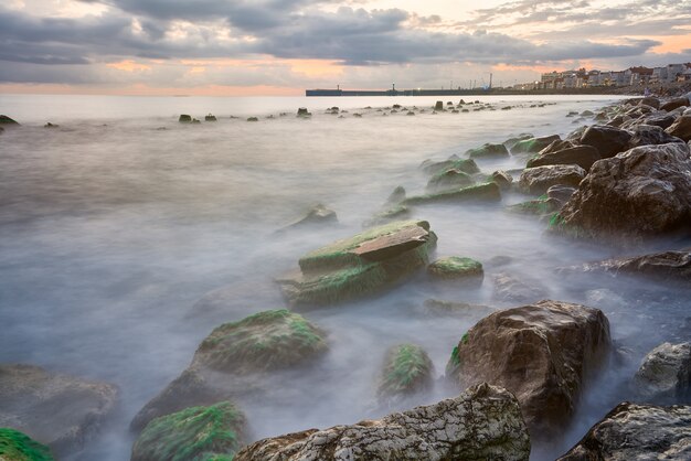 Coastal landscape with warm evening light when waves break on rocks covered with seaweed