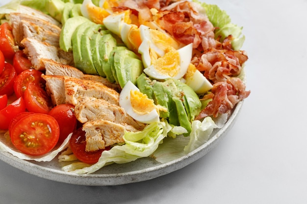 Cobb salad with bacon avocado tomato grilled chicken eggs on white background American food