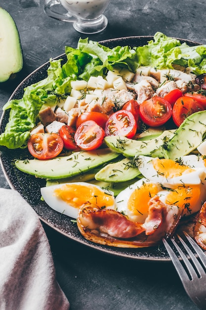 Cobb salad with chicken, avocado, tomatoes, eggs, bacon and cheese on a black  table close up.