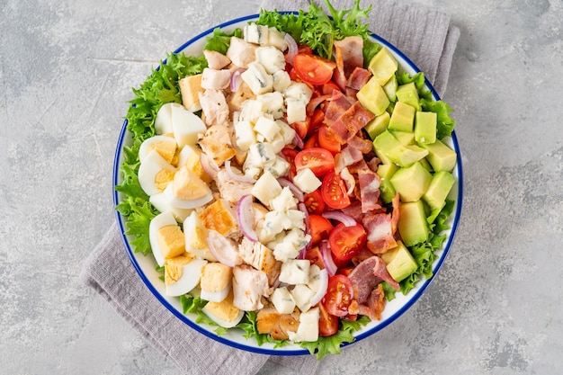 Cobb salad with fried chicken avocado fresh tomatoes egg bacon and cheese on a plate selective focus