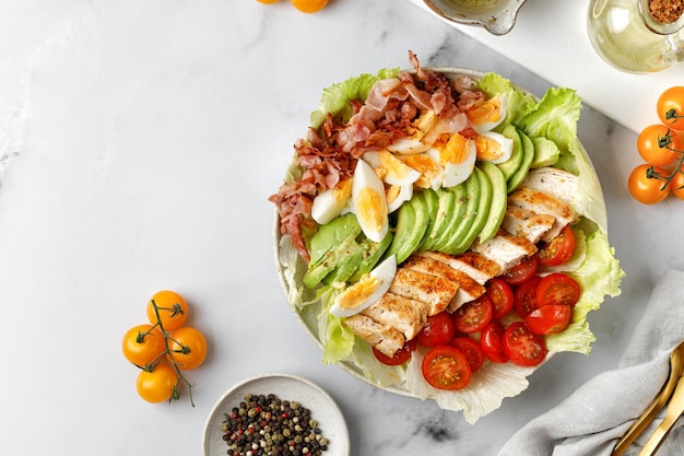 Cobb salad with grilled chicken eggs avocado tomato bacon on marble white background Keto diet