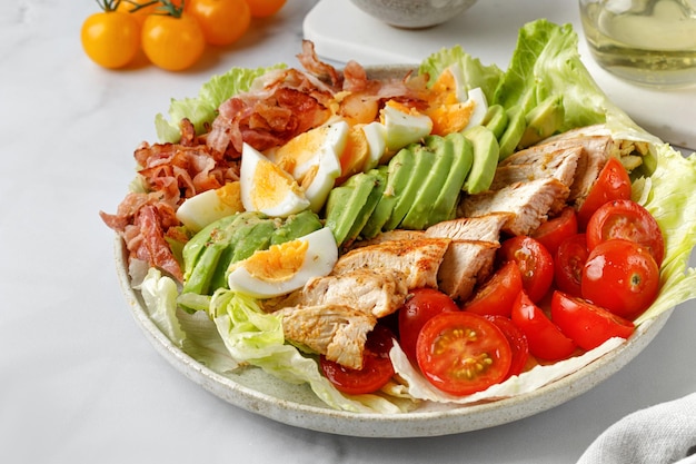 Cobb salad with grilled chicken eggs avocado tomato bacon white background Classic American salad 