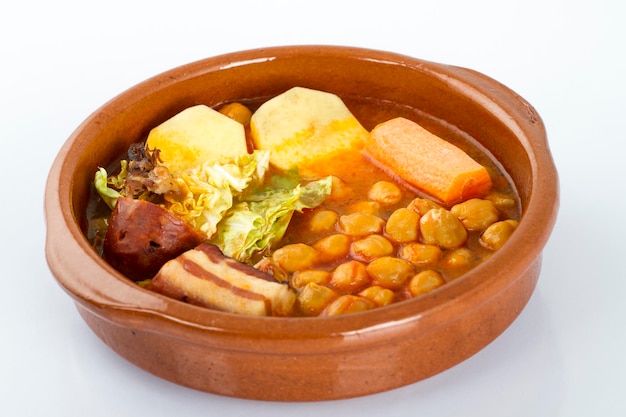 Cocido de Madrid, traditional Spanish dish with chickpeas. meat, sasuages, and vegetables, in a typical dish, isolated on white