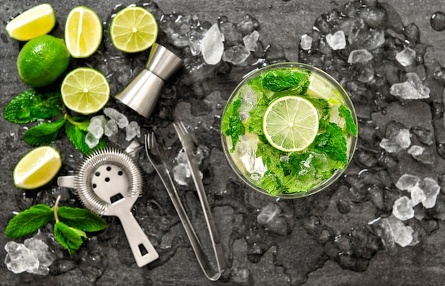 Cocktail juice with lime, mint and ice. Bar drink accessories on black table background. Alcoholic and nonalcoholic cold drinks. Selective focus