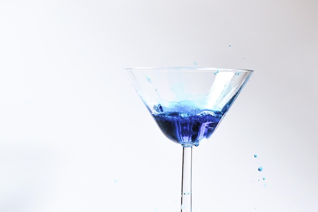 Cocktail with blue liquid in glass Glass with blue water pouring with liquid with splashes and drops Martini glass filling with alcohol with splashes on white background Refreshing drink concept