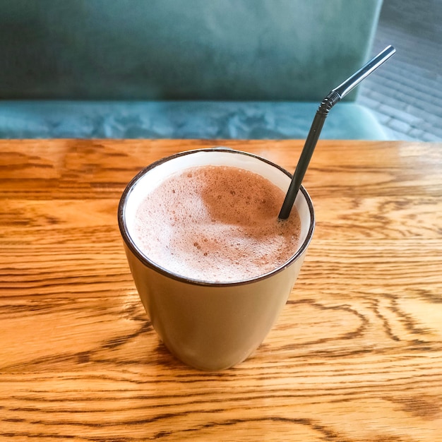 Cocoa drink with a straw in ceramic mug on wooden table in a cafe