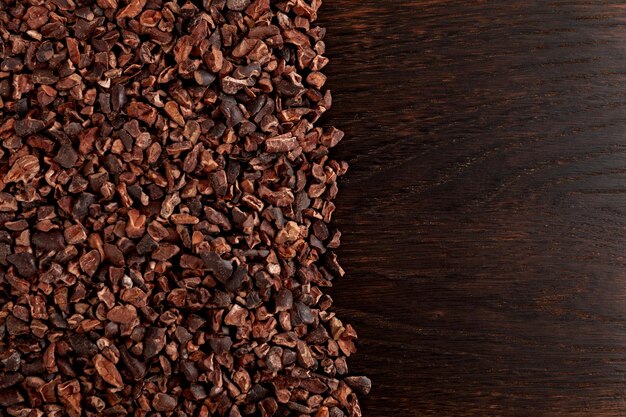 Cocoa nibs on brown wooden surface, closeup. Cocoa nibs used to make a hot drink.