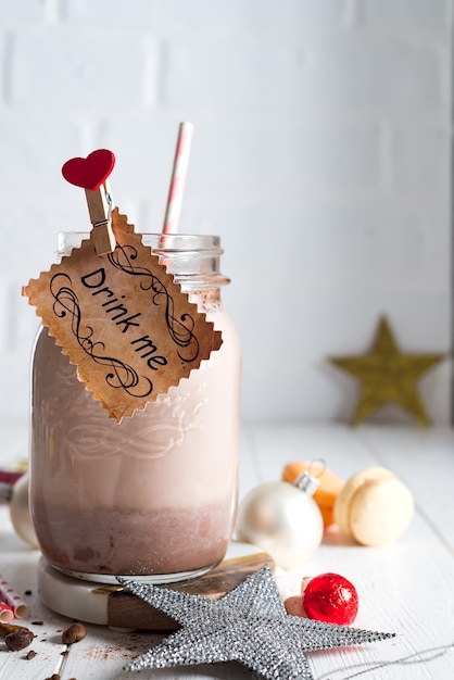 Cocoa with marshmallow and straws in the glass jar with a sign Drink me decorated 